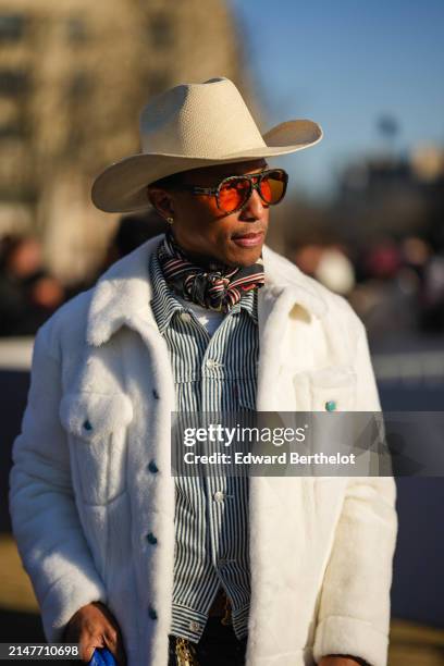 Pharrell Williams wears sunglasses , a white cowboy hat, a scarf, a black and white striped shirt, a white fluffy coat, outside Dior, during the...