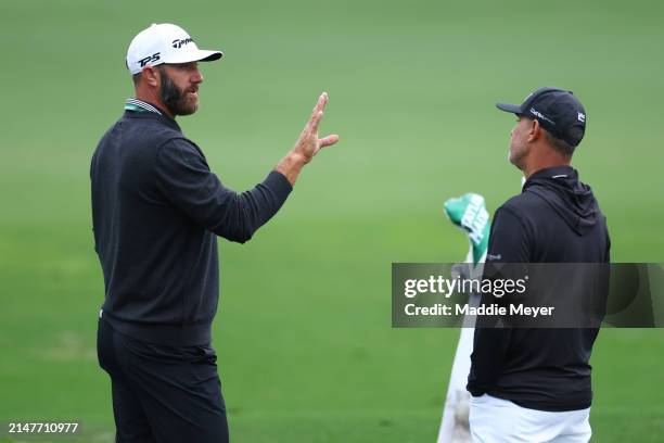 Dustin Johnson of the United States speaks with coach Claude Harmon III in the practice area prior to the 2024 Masters Tournament at Augusta National...