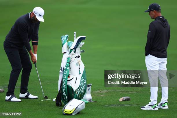 Dustin Johnson of the United States plays a shot as coach Claude Harmon III looks on in the practice area prior to the 2024 Masters Tournament at...