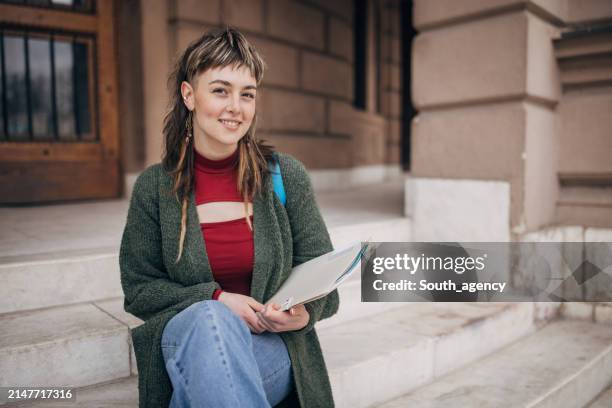 lächelnder student mit notizbuch auf den stufen des campus - studierendenvertretung stock-fotos und bilder