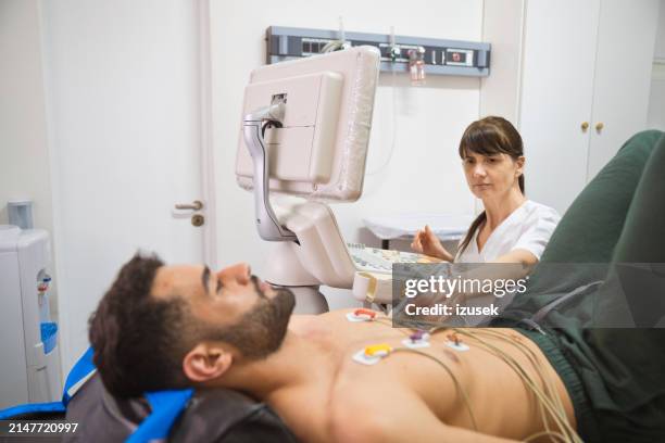 arzt, der ekographie eines männlichen patienten ohne hemd im untersuchungsraum durchführt - kardiologe stock-fotos und bilder