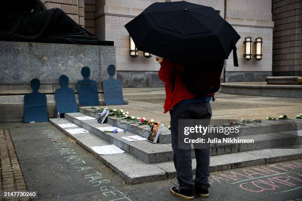 Person looks at flowers and signs on the ground in front of the U.S. Agency for International Development building at a vigil for aid workers killed...