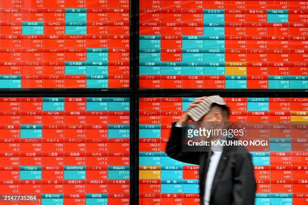 Man walks past an electronic board displaying stock prices of Nikkei 225 listed on the Tokyo Stock Exchange along a street in Tokyo on April 12, 2024.