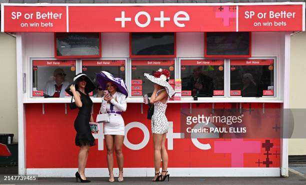 Racegoers stand at a betting office window ahead of racing on the second day of the Grand National Festival horse race meeting at Aintree Racecourse...
