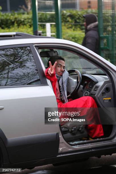 An activist wearing the red jumpsuit of Palestine Action gives the V peace sign as he sits attached to the car steering wheel by a D-lock around his...