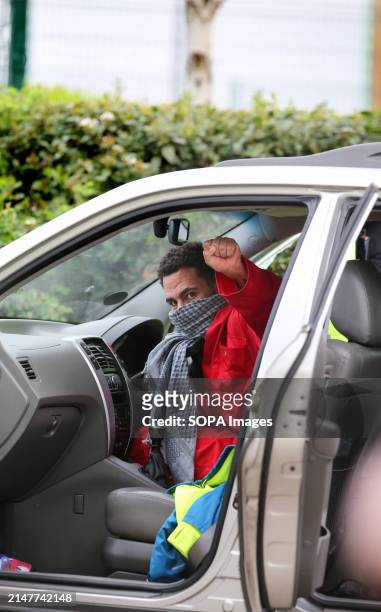 An activist wearing the red jumpsuit of Palestine Action gives a raised fist as he sits attached to the car steering wheel by a D-lock around his...