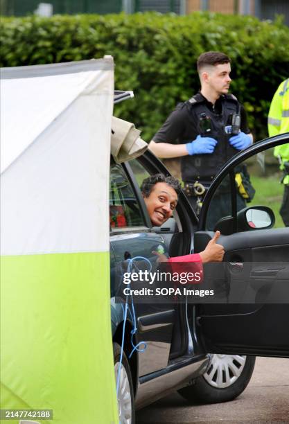 An activist wearing the red jumpsuit of Palestine Action gives the thumbs-up as he sits attached to the car steering wheel by a D-lock around his...