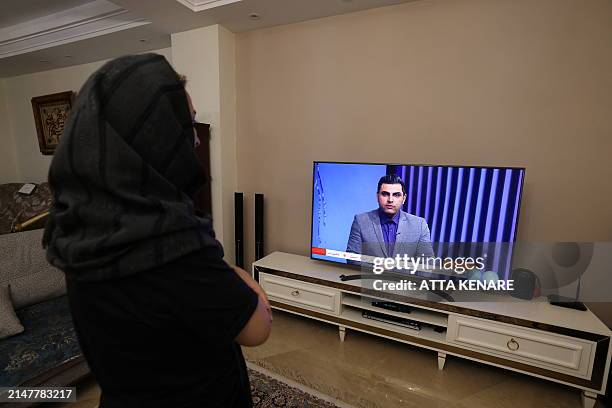 An Iranian woman in Tehran watches an Iranian news TV channel, which is covering the news of Iran's attack on Israel, on April 14, 2024. Israel was...