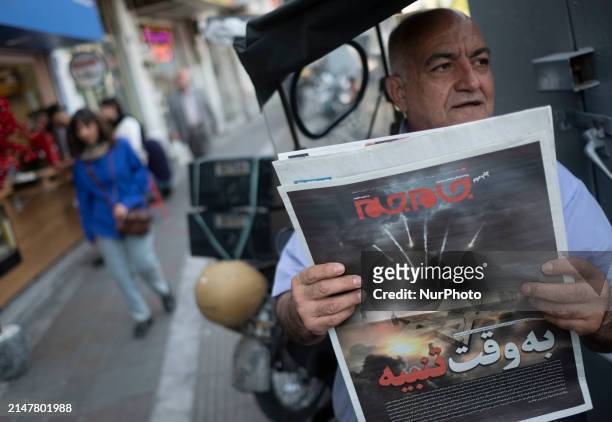 An Iranian man is sitting on a sidewalk in downtown Tehran, Iran, on April 14 holding a Jam-e Jam daily newspaper that features an illustrated image...
