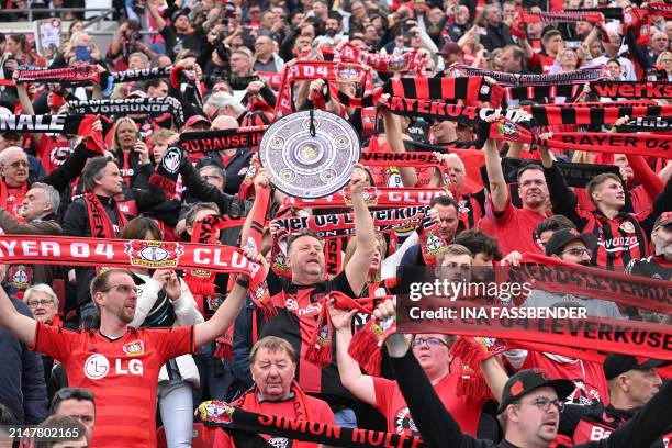 One Leverkusen fan displays a mock-up of the Bundesliga trophy as they cheer prior to the German first division Bundesliga football match Bayer 04...