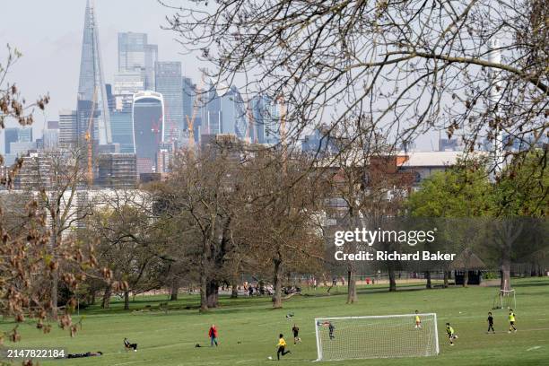 With the skyscrapers of the City of London, tha capital's financial district in the far distance, junior youth teams play a game of football on a...