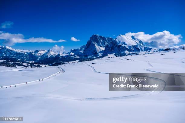 Hilly agricultural countryside with snow-covered pastures and cross-country ski trails at Seiser Alm in winter, summits of Sassolungo and Sasso...