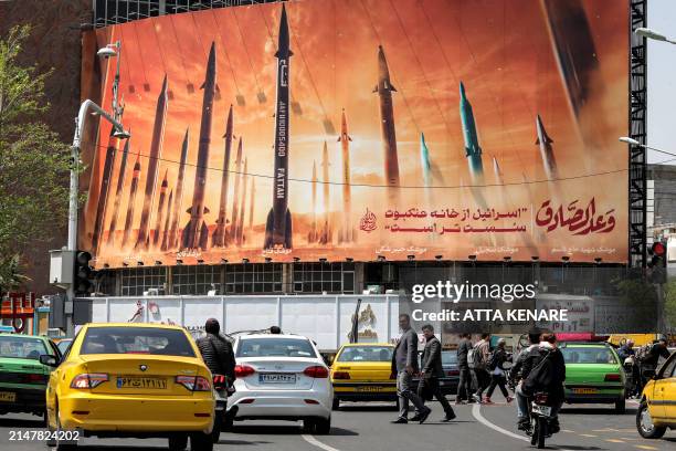 Motorists drive their vehicles past a billboard depicting named Iranian ballistic missiles in service, with text in Arabic reading "the honest...