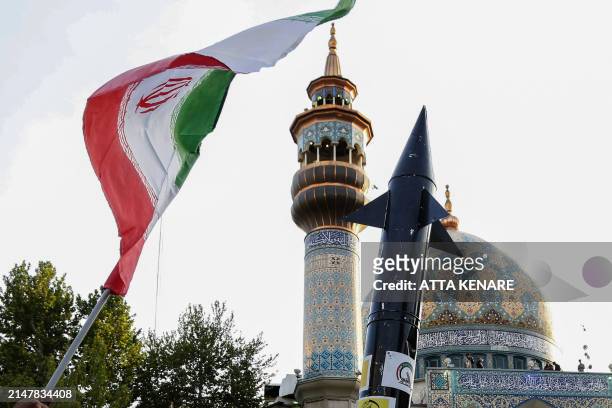 Iranians lift up a flag and the mock up of a missile during a celebration following Iran's missiles and drones attack on Israel, on April 15 2024, at...