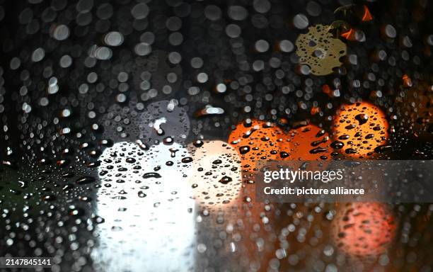 Dpatop - 16 April 2024, Baden-Württemberg, Stuttgart: Lights from vehicles shine through a car windshield covered with raindrops. Photo: Bernd...