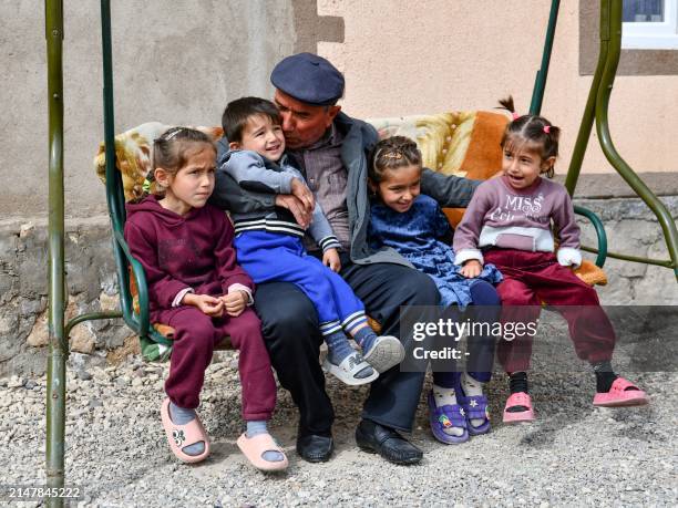 Djamoliddine Makhmaliev sits with his grandson and granddaughters in front of his new house in the village of Khuroson, near Obikiik, some 70...