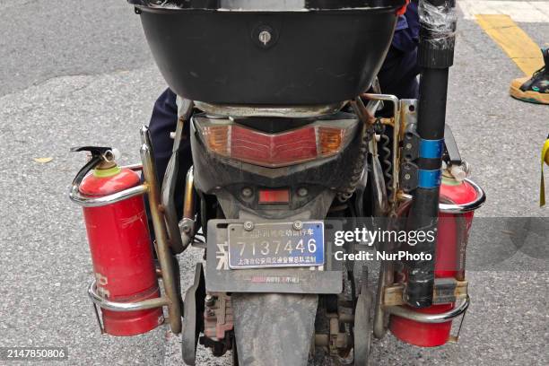 Man is riding a two-wheeled electric bicycle equipped with two fire extinguishers and warning poles, and is wearing a work vest that reads...