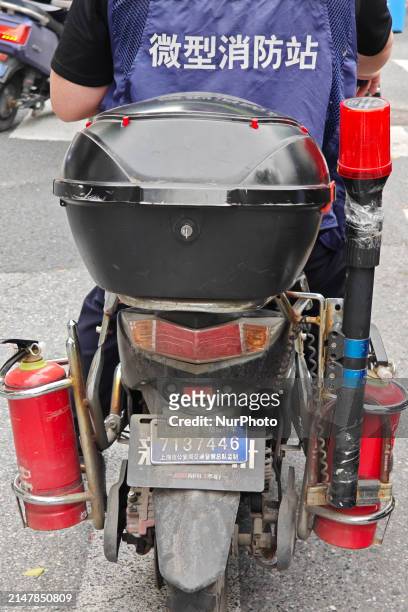 Man is riding a two-wheeled electric bicycle equipped with two fire extinguishers and warning poles, and is wearing a work vest that reads...
