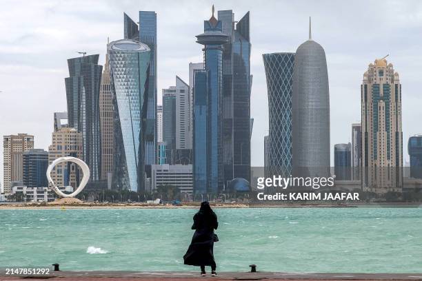 Woman stands by the waterfront at the Doha corniche facing the high-rise buildings in the West Bay district on April 16, 2024.