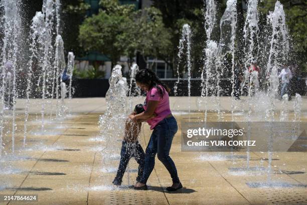 Woman and her child cool off at a water fountain in the Monumento a la Revolucion square during a heat wave that hits Mexico City on April 16, 2024....