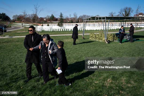 Arlington, VA Rosana Monge, her son Joseph, and grand children Jax help her as they walk away from the casket of Joe Monge during a burial service at...
