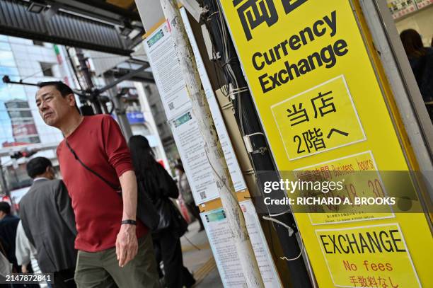 Pedestrians walk past a currency exchange shop in central Tokyo on April 17 as the yen continues its downward spiral against the US dollar. The...