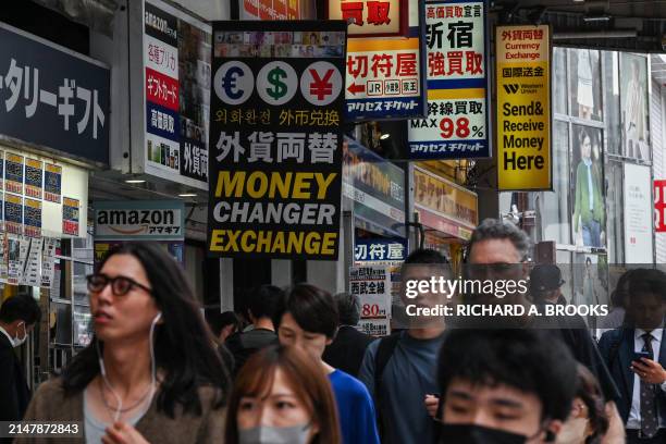 Pedestrians walk past a line of currency exchange shops in central Tokyo on April 17 as the yen continues its downward spiral against the US dollar....