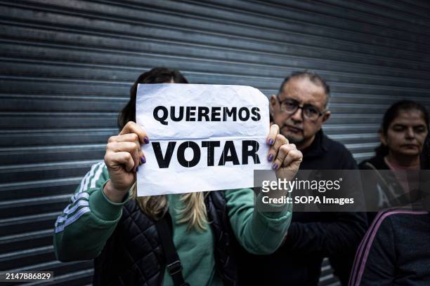 Young Venezuelan woman holds a sign saying "We want to vote" at the door of the closed Embassy during the demonstration. A group of Venezuelan...
