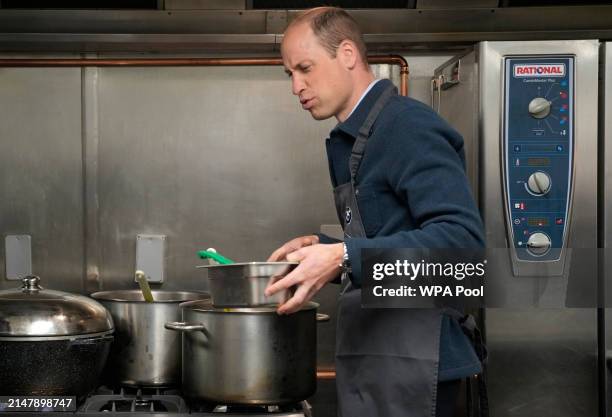 Prince William, Prince of Wales reacts as he helps make bolognese sauce with head chef Mario Confait during a visit to Surplus to Supper, in...