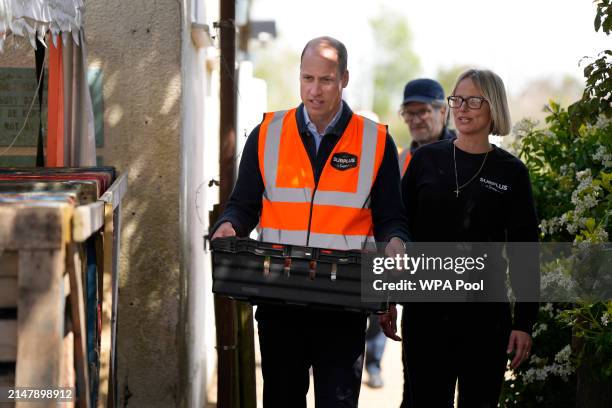 Prince William, Prince of Wales carries a tray of food items while talking to Claire Hopkins, Operations Director, during a visit to Surplus to...