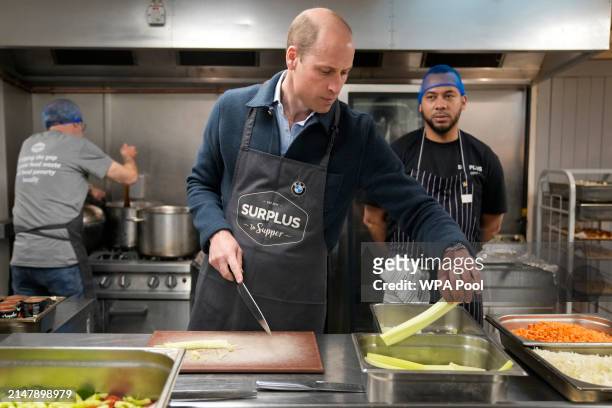 Prince William, Prince of Wales speaks with head chef Mario Confait, as he cuts celery while helping to make a bolognese sauce during a visit to...