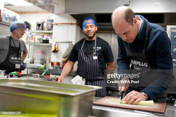 Prince William, Prince of Wales speaks with head chef Mario Confait, as he cuts celery while helping to make a bolognese sauce during a visit to...