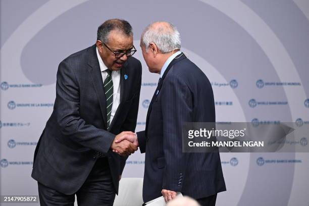 Japanese Finance Minister Shun'ichi Suzuki shakes hands with World Health Organization Director-General Tedros Adhanom Ghebreyesus during an event...