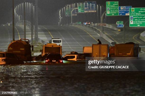 Person sits of the roof of a lorry as vehicles are stranded in flood waters along a highway in Dubai following heavy rains on April 18, 2024. Dubai's...