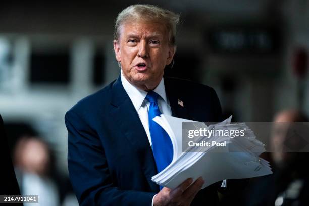 Republican presidential candidate, former President Donald Trump holds print outs of news stories as he speaks to reporters at the end of the day as...