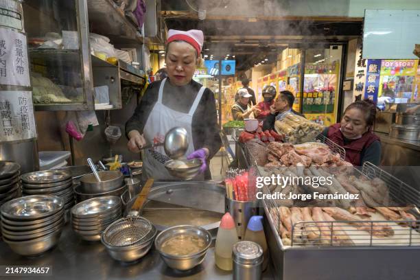 Street vendor attentively prepares a dish by the roadside with a variety of meat on display.