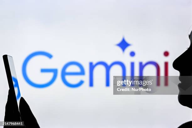 An image of a woman holding a cell phone in front of a Gemini logo displayed on a computer screen, on April 20 in Edmonton, Canada.