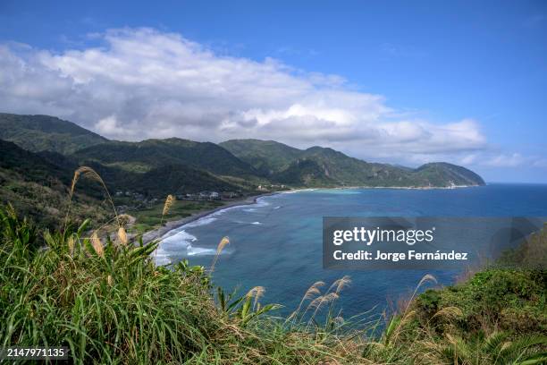 Sweeping coastal landscape with a small seaside village nestled among lush hills under a bright sky.