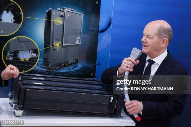German Chancellor Olaf Scholz speaks into a cable next to a fuel cell as he visits the booth of German electronic connector manufacturer Harting...