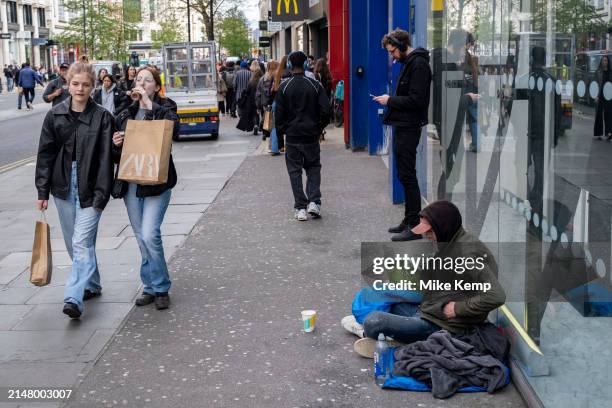 Person sitting on the pavement under a sleeping bag while people pass by on Oxford Street on 11th April 2024 in London, United Kingdom. The scene is...
