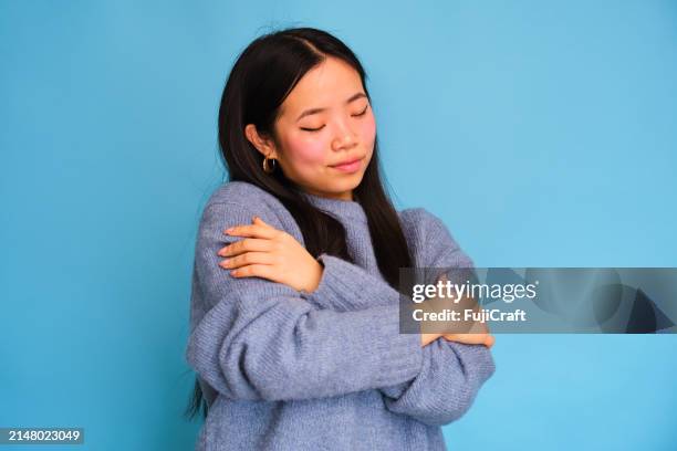 a woman in a blue sweater is hugging herself. - low self esteem stock pictures, royalty-free photos & images