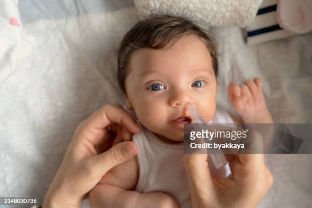 close up of caring mother with nasal pump to clean her baby's nose. baby lying in bed - nasal passage stock pictures, royalty-free photos & images