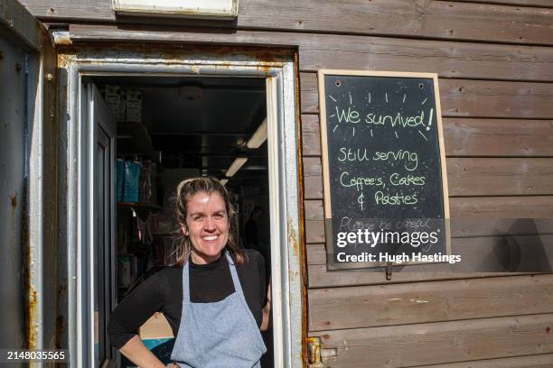 Chloe Carrick, a staff member at Castle Beach Cafe, next to signage outside the cafe, which opened the day after three beach huts were swept into the...