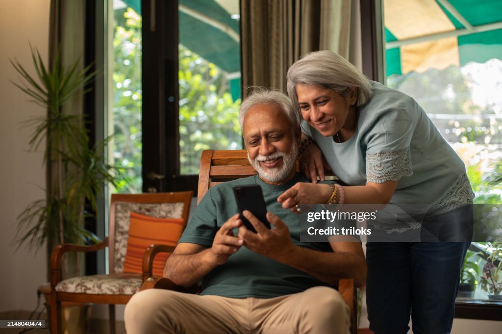 Pareja de ancianos que usa las redes sociales a través del teléfono celular en casa