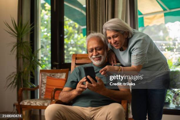 senior couple using social media over cellphone at home - indiskt ursprung bildbanksfoton och bilder