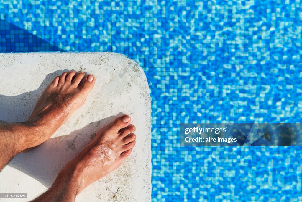 High angle view of a man's bare feet standing on a pool diving board preparing to jump into the water