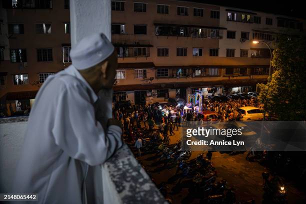 Man watches as people march alongside a decorated moving platform while chanting takbir ahead of Eid al-Fitr on April 09, 2024 in Selangor, Malaysia....