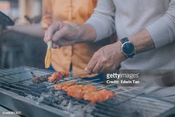 close up chinese senior man brushing honey on satay experience in local penang restaurant - brazier stock pictures, royalty-free photos & images