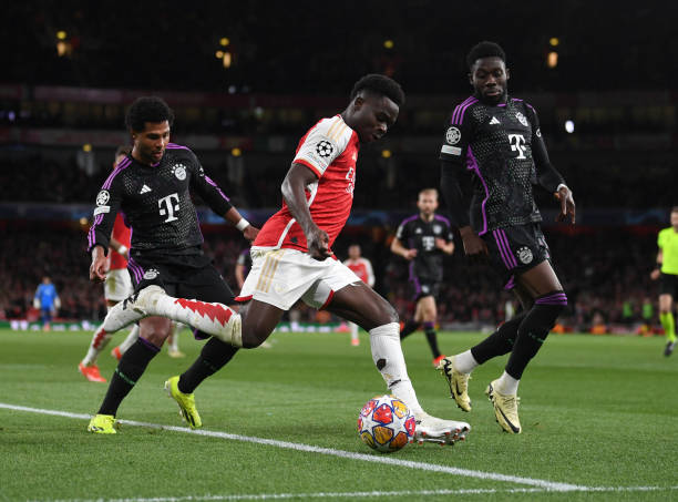 Bukayo Saka of Arsenal crosses the ball under pressure from Serge Gnabry and Alphonso Davies of Bayern during the UEFA Champions League quarter-final...