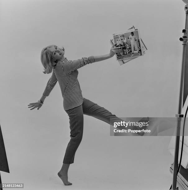 Posed studio portrait of a female fashion model wearing a striped top and cropped Capri pants, she holds a selection of long playing records in one...